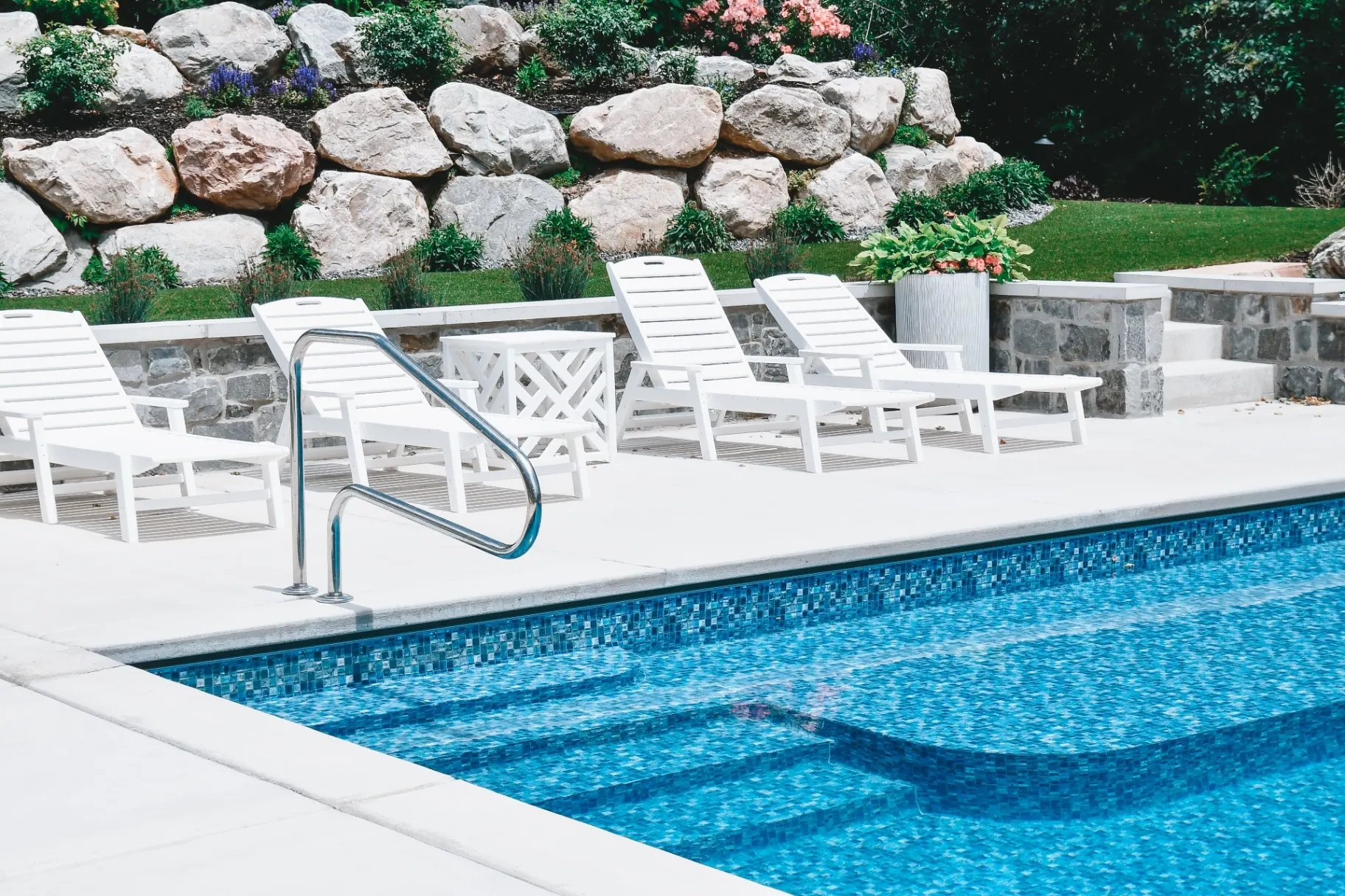 Kaysville Utah Mosaic-Tile Vinyl Pool with Lounge - Barr Pool Builders Blue mosaic-tile inground vinyl swimming pool with poolside lounge chairs and boulder wall in Kaysville, Utah by Barr Pool Builders