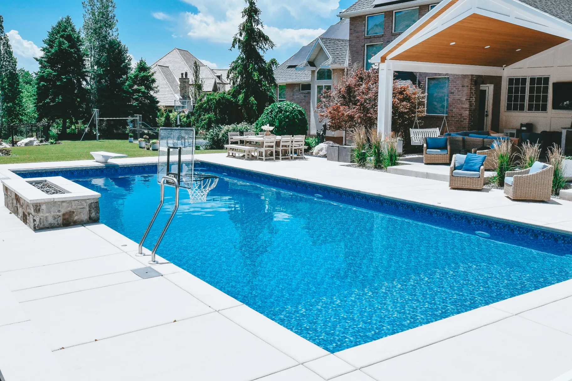 Layton Utah Luxury Vinyl Pool with Basketball Hoop & Firepit - Barr Pool Builders Luxury vinyl swimming pool with in-pool basketball hoop, diving board and stone firepit in a Layton, Utah backyard built by Barr Pool Builders